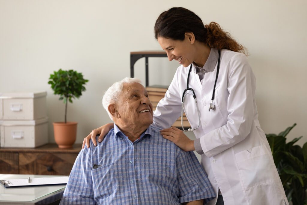 Optimistic young lady doctor embrace shoulders of laughing old man sitting on chair at clinic office